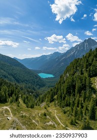 Aerial view of alpine lake Lago di Anterselva (Antholzer See) as seen from Passo Stalle (Staller Pass) in a Dolomite mountain valley with green pine forest 