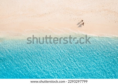 Aerial view of amazing beach with couple walking in sunset light close to turquoise sea. Top view of summer beach landscape, romantic love couple vacation, romantic holiday. Freedom leisure activity