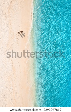 Aerial view of amazing beach with couple walking in sunset light close to turquoise sea. Top view of summer beach landscape, romantic love couple vacation, romantic holiday. Freedom leisure activity