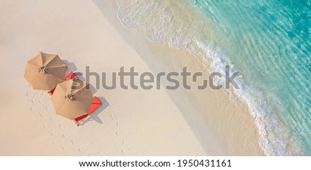 Aerial view of amazing beach with umbrellas and lounge chairs beds close to turquoise sea. Top view of summer beach landscape, idyllic inspirational couple vacation, romantic holiday. Freedom travel
