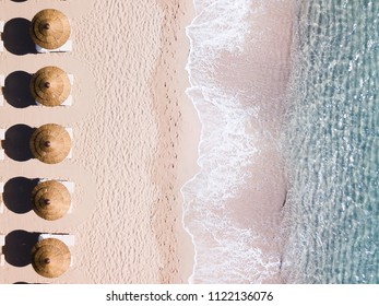 Aerial view of amazing turquoise sea with brown straw umbrellas and sun loungers. Beautiful sunny summer day in Sardinia, Mediterranean sea, Italy. 