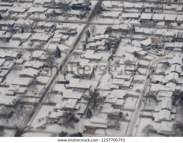 Aerial view of an\
American neighborhood in winter. Most houses are modest ranch and\
split level, but a large home is being built in the corner lot\
missing half the roof