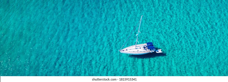 Aerial View Of Anchored Sailing Yacht In Emerald Sea. Aerial View Of A Boat. Outdoor Water Sports, Yachting. Aerial View Of Anchoring Yacht In Open Water. Ocean And Sea Travel And Transportation