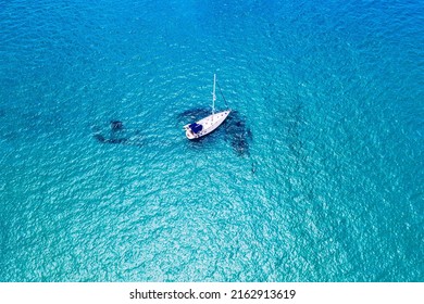 Aerial View Of Anchored Sailing Yacht In Emerald Sea. Aerial View Of A Boat. Outdoor Water Sports, Yachting. Aerial View Of Anchoring Yacht In Open Water. Ocean And Sea Travel And Transportation