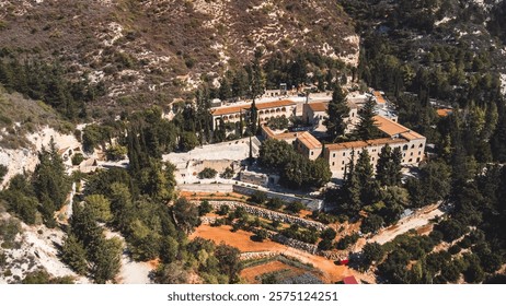 Aerial view of an ancient monastery surrounded by lush greenery and rugged mountains in Cyprus, showcasing historical architecture and natural beauty.
