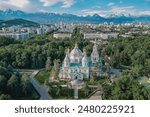 Aerial view of the Ascension Cathedral Russian Orthodox church and snow mountains at background in Panfilov Park against blue sky in Almaty city, Kazakhstan