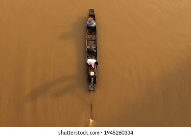 Aerial View An Asian Fisherman Stands On Traditional Wooden Fishing Boat While Casting Fishing Net On A River At Sunrise. Rural Scene In Thailand. Focus On Fisherman.