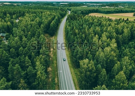 Aerial view of asphalt road with cars through green summer woods in Finland