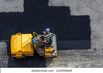 Aerial View Of Asphalting Construction Works With Commercial Repair Equipment Road Parking For The Car With Yellow Roller Compactor Machine. Contrast Between New And Old Road Surface