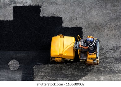 Aerial View Of Asphalting Construction Works With Commercial Repair Equipment Road Parking For The Car With Yellow Roller Compactor Machine. Contrast Between New And Old Road Surface