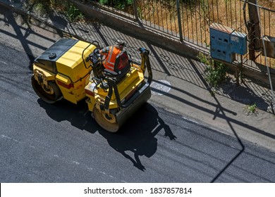 Aerial View Of Asphalting Construction Works With Commercial Repair Equipment Road Parking For The Car With Yellow Roller Compactor Machine. Contrast Between New And Old Road Surface