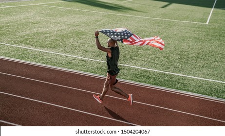 Aerial view of an athlete running on athletic track holding the american flag over the head - Powered by Shutterstock