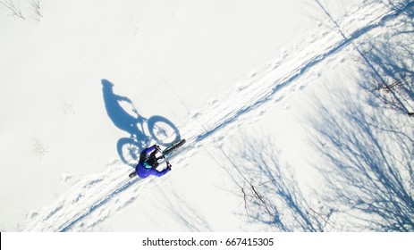 An Aerial View Of An Attractive Woman Riding Their Fat Bikes On A Trail In The Snow.