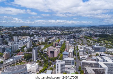 Aerial View Of Auckland, New Zealand City Scape With Urban Buildings, Green Trees And Clouds In The Sky