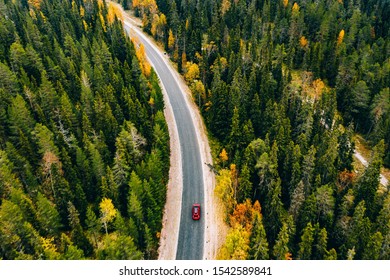 Aerial view of autumn color forest in the mountains and a road with red car in Finland Lapland.