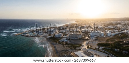 Aerial view of Ayia Napa, Cyprus, featuring Nissi and Landa Beaches, turquoise waters, luxury hotels, a small harbor, and a vibrant coastal town.