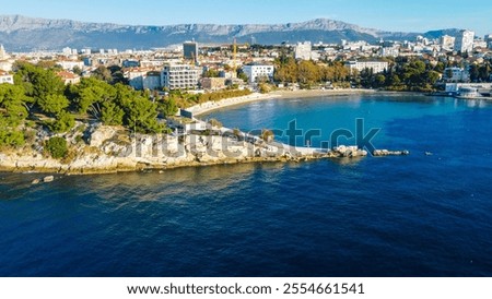 Aerial view of Bacvice Beach in Split, Croatia, showcasing the sandy beach, clear blue water, and vibrant atmosphere, with people enjoying the sunny weather and the stunning coastal landscape