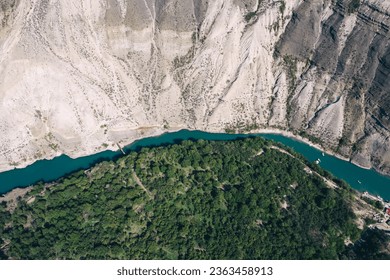 Aerial view of barren mountain and valley with river used by boats while green vegetation with trees and roads of countryside visible under bright sunshine during summertime