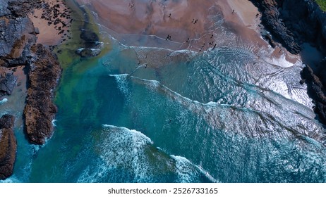 Aerial view of a beach with clear blue waters and sandy shores. Waves gently crash on the shore, creating a beautiful contrast with the rocky formations. At Porth Beach, Cornwall, UK. - Powered by Shutterstock