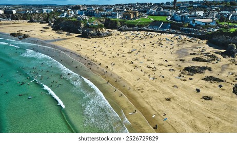 Aerial view of a beach with golden sand and clear turquoise water. Numerous people are enjoying the sun, swimming, and surfing. At Towan Beach, Newquay, Cornwall, UK. - Powered by Shutterstock