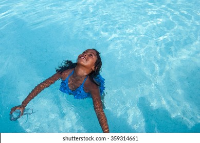 Aerial View At Beautiful Brazilian Girl Wearing Blue Swimsuit With Diving Goggles 
Smiling Female Child Swimming In A Pool With Clear Water On A Sunny Day