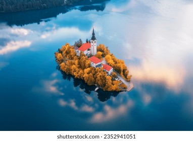 Aerial view of beautiful church and buildings on the island on the famous Bled Lake, Slovenia in autumn morning. Top drone view of chapel, houses, orange trees, blue water in fall. Landscape. Travel - Powered by Shutterstock