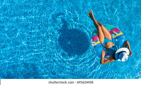 Aerial view of beautiful girl in swimming pool from above, relax swim on inflatable ring donut and has fun in water on family vacation
