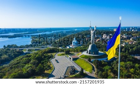Aerial view to the  Beautiful landscape city Kiev with a Dnepr river. Top view to the Motherland statue in the Kiev. The well-known landmarks in Kyiv. Closeup National flag og Ukraine.