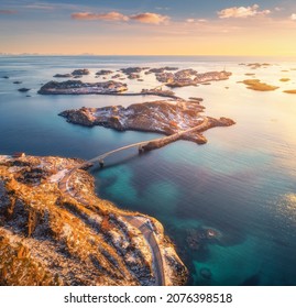 Aerial View Of Beautiful Mountains, Bridge, Small Islands In The Sea, Road, Orange Sky At Sunset. Lofoten Islands, Norway In Winter. Top View Of Road, Snowy Rocks, Stones, Sea Coast, Water. Top View