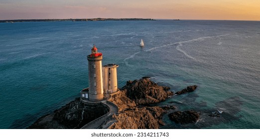 An aerial view of a beautiful seascape with a white lighthouse and a sailboat in the background - Powered by Shutterstock