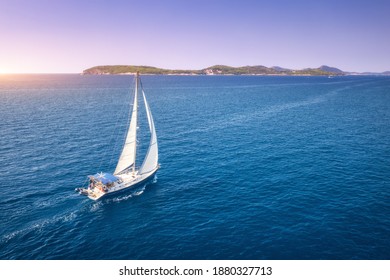 Aerial view of beautiful white sailboat in blue sea at bright sunny summer evening. Adriatic sea in Croatia. Landscape with yacht, mountains, transparent blue water, sky at sunset. Top view of boat