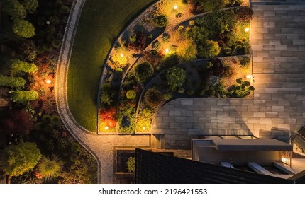 Aerial View Of Beautifully Designed And Landscaped Garden On The Backyard Of Residential House. Garden Path And Terrace Surrounded By Variety Of Plants Enlightened By Solar Lamps. Evening Time.