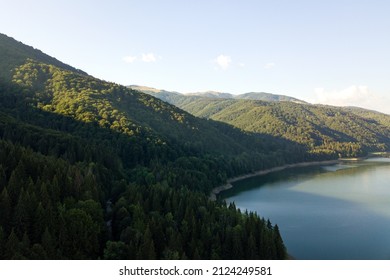 Aerial view of big lake with clear blue water between high mountain hills covered with dense evergreen forest.