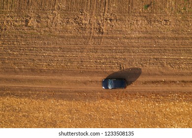 Aerial View Of Black Car On Dirt Road Through Countryside, Top View Of Off-road Driving Vehicle From Drone Pov