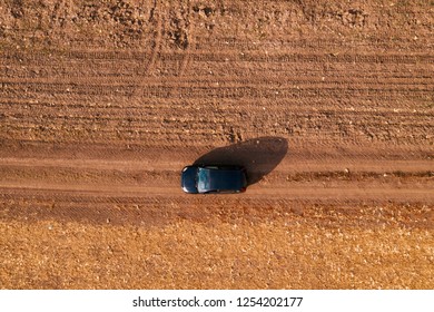 Aerial View Of Black Car On Dirt Road Through Countryside, Top View Driving Vehicle From Drone Pov