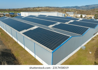 Aerial view of blue photovoltaic solar panels mounted on industrial building roof for producing green ecological electricity. Production of sustainable energy concept - Powered by Shutterstock