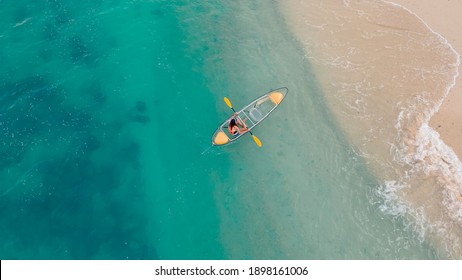 aerial view of blue sea with floating transparent kayak is going into sand beach, person with life jacket on boat