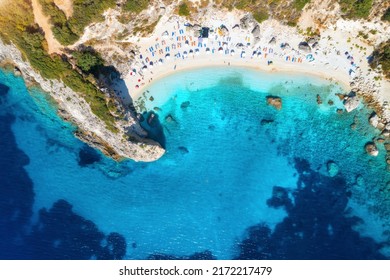 Aerial view of blue sea, rock, sandy beach with umbrellas at sunrise in summer. Porto Katsiki, Lefkada island, Greece. Beautiful landscape with sea coast, swimming people, trees, azure water. Top view