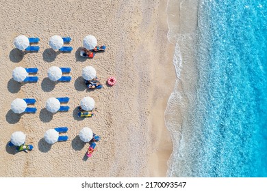 Aerial view of blue sea, sandy beach with sun beds and umbrellas at sunset in summer. Tropical landscape with clear water, people, deck chair. Travel and vacation. Lefkada island, Greece. Top view - Powered by Shutterstock