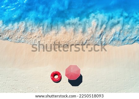 Aerial view of blue sea with waves and empty white sandy beach with red swim ring and umbrella at sunset in summer in Zanzibar, Africa. Tropical landscape with sand and azure water. Ocean. Top view