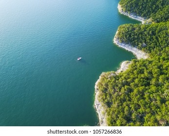 Aerial view bluffs with small boat at Lake Travis, Austin, Texas, USA. Trees, cliff rock wall coming out of water from above. Blue ocean crystal, moderate waves looking straight down, green forest