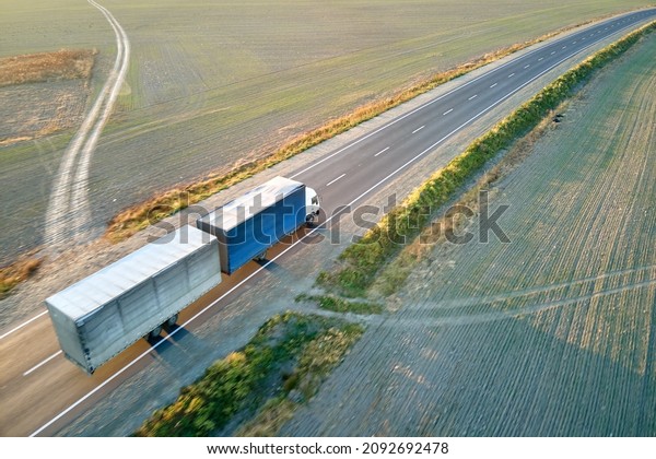 Aerial view of blurred fast moving\
semi-truck with cargo trailer driving on highway hauling goods in\
evening. Delivery transportation and logistics\
concept