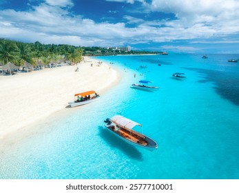 Aerial view of the boats on tropical sea coast with white sandy beach on summer sunny day. Vacation in Kendwa, Zanzibar. Landscape with boat, yacht, clear water, green palms, blue sky. Top drone view