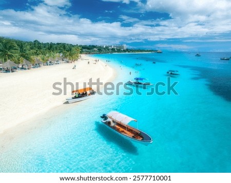 Aerial view of the boats on tropical sea coast with white sandy beach on summer sunny day. Vacation in Kendwa, Zanzibar. Landscape with boat, yacht, clear water, green palms, blue sky. Top drone view