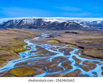 Aerial view of braided river in Iceland with snow-capped mountains and vibrant landscape under a clear blue sky. - Powered by Shutterstock