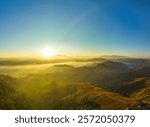 Aerial view of A breathtaking aerial view of a lush, green mountain range under a bright, clear blue sky, with sunlight illuminating the vast, rolling terrain and valleys below.