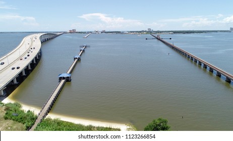 An Aerial View Of A Bridge, Highway, And Pier On The Coast Of Florida. The Highway Extends Into Pensacola Beach With Gulf Breeze On The Other Side.