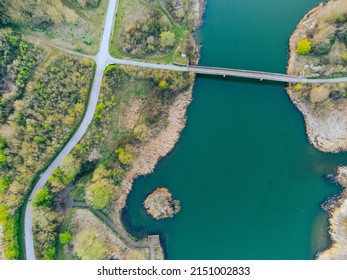 An aerial view of a bridge over a lake connected to an island full of autumn trees 