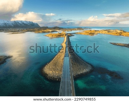 Aerial view of bridge over the sea and snowy mountains in Lofoten Islands, Norway. Fredvang bridges at sunset in winter. Landscape with blue water, rocks in snow, road, sky with clouds. Top drone view