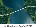 Aerial view of bridge road with red car over blue water lake or sea with island  and green woods in summer Finland.
